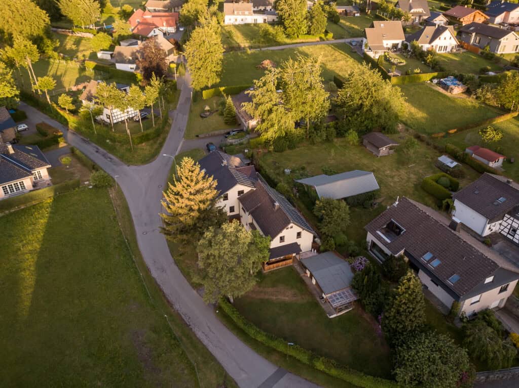 Luftaufnahme eines ruhigen Vorortviertels in der Eifel, perfekt für einen Familienurlaub in der Eifel, mit Häusern, grünen Rasenflächen, Bäumen und kurvigen Straßen an einem sonnigen Tag.